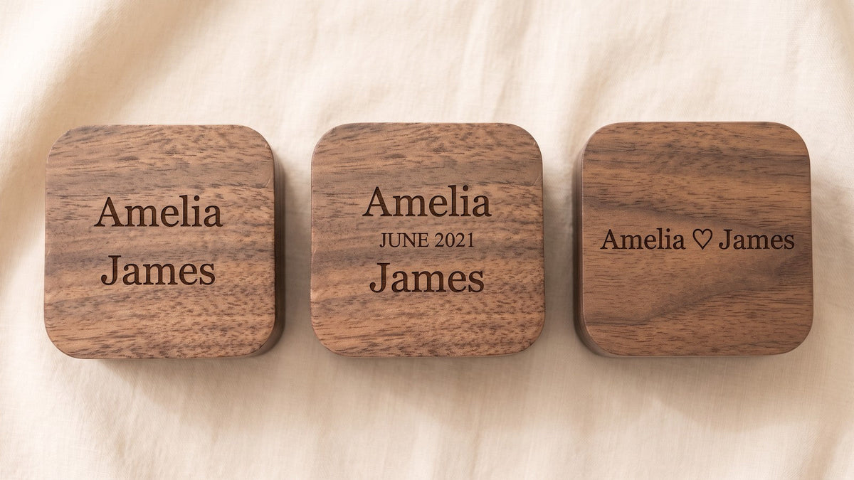 Three walnut ring box lids engraved with the same two names in three different layouts: two lines, three lines with a date, and one line with a heart symbol