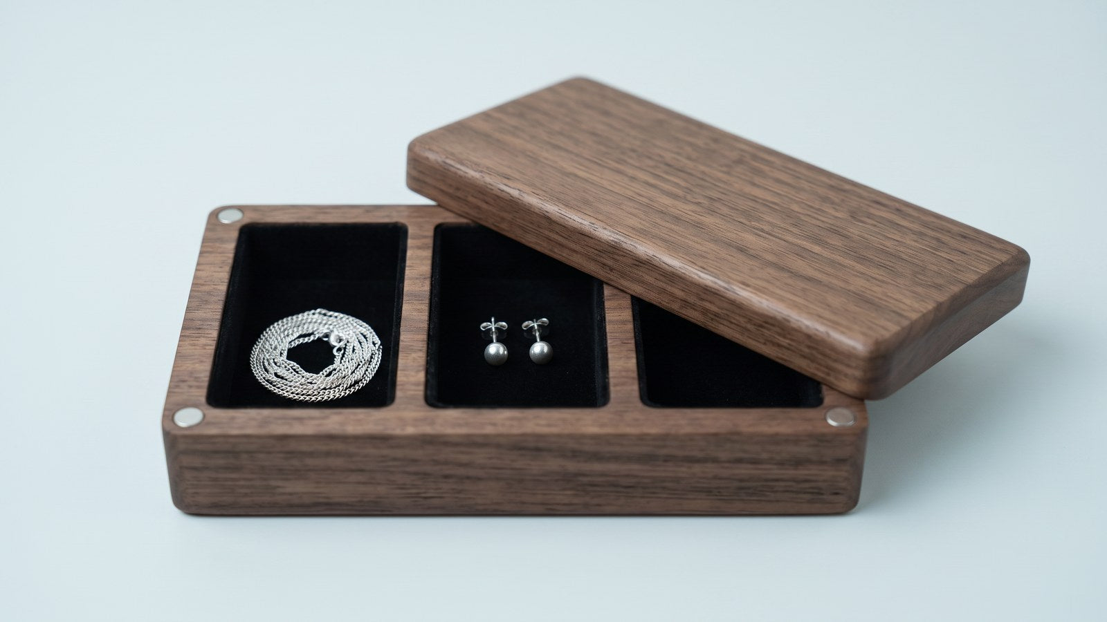 Sterling silver chain and silver studs stored in the black velvet compartments of a walnut stud earring box
