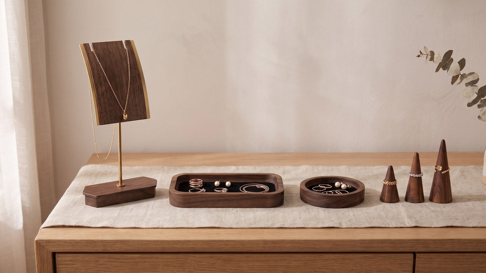 Walnut necklace stand, rectangular jewelry tray, round ring dish and three ring cones arranged along a dresser top
