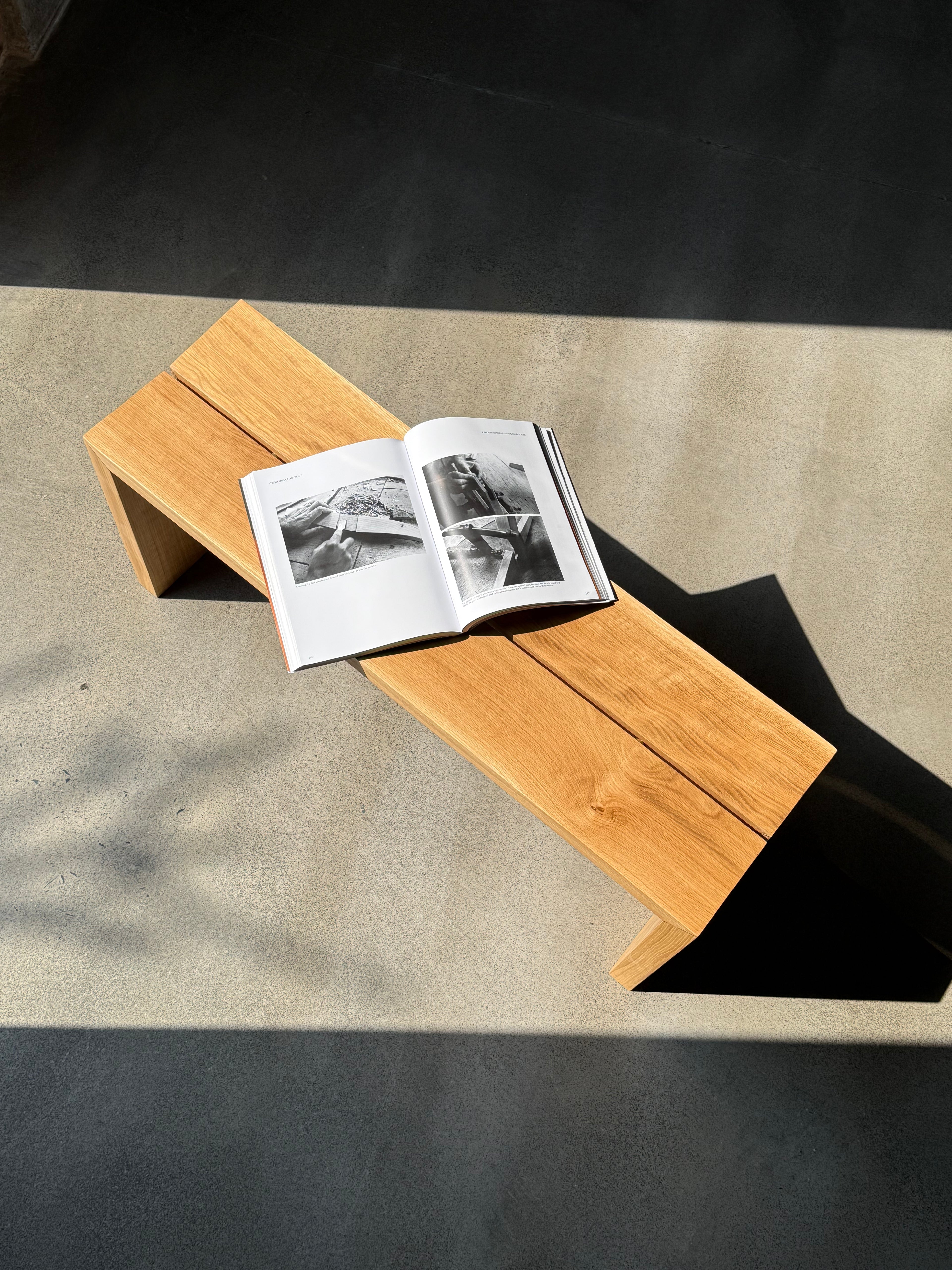 White oak bench with split top beam and open shelf, magazine on seat