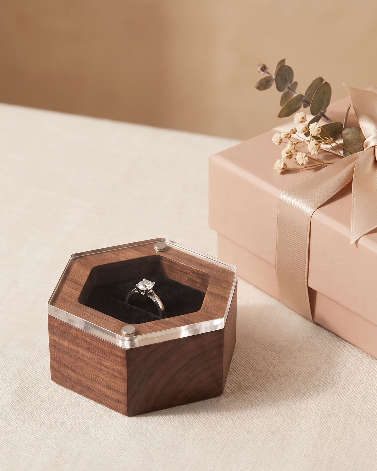 Hexagonal black walnut wedding ring box with clear acrylic lid beside a ribboned gift box