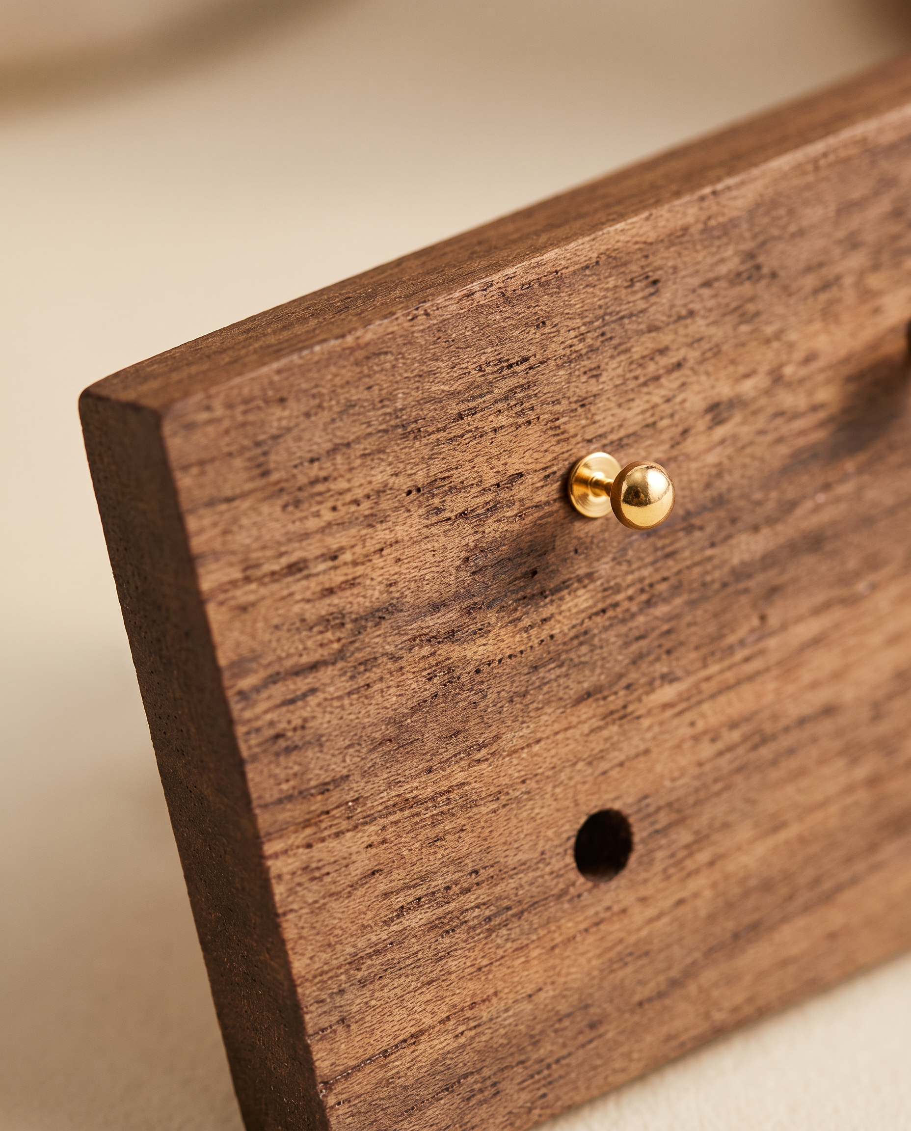 Walnut earring holder close-up with two brass posts and visible drilled hole