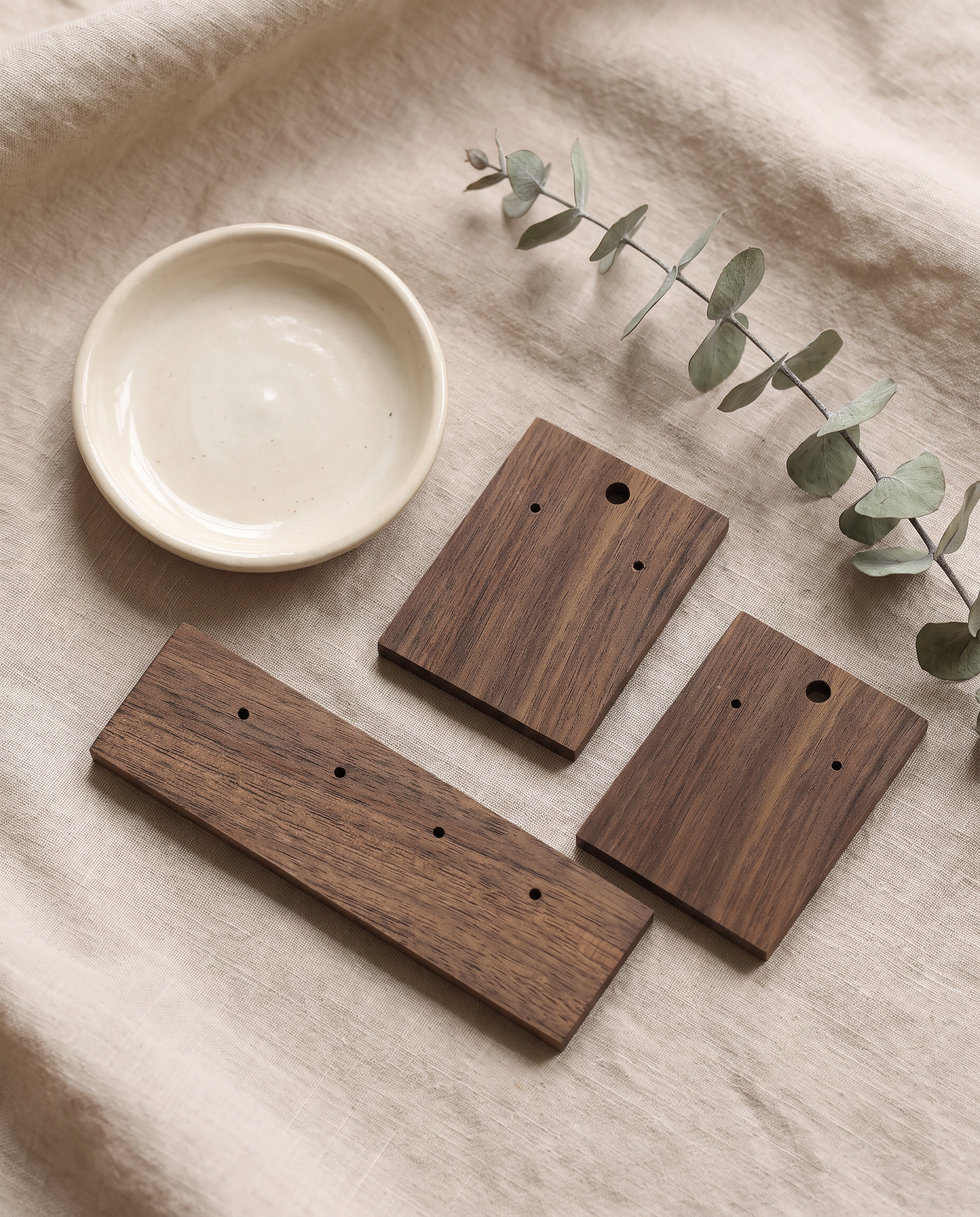 Walnut earring holder boards with eucalyptus sprigs and earrings, dark wood with holes