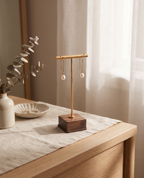 Gold T-bar earring stand with walnut base, holding two dangling pearl earrings