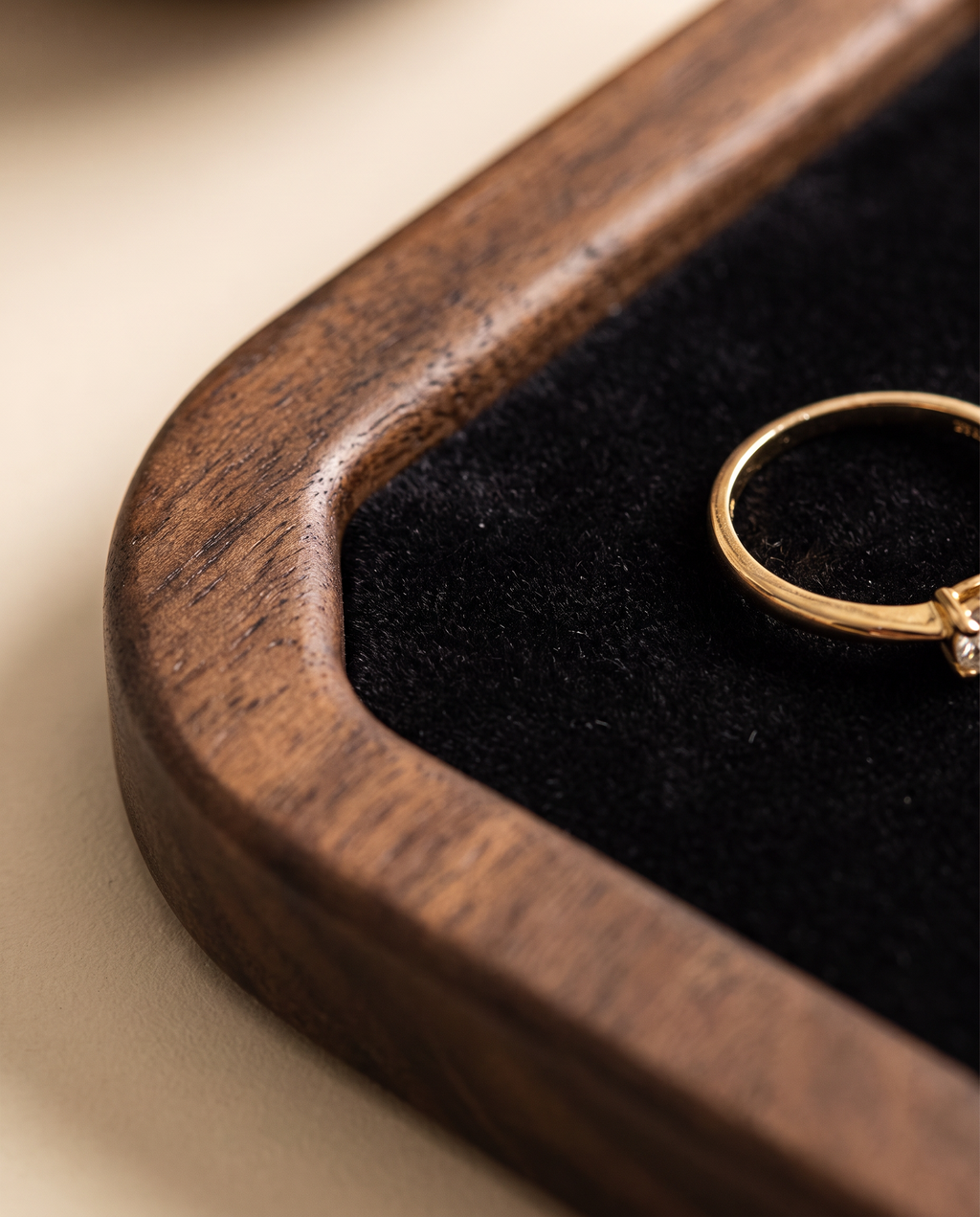 Walnut edge of a square jewelry tray with dark velvet and a gold ring