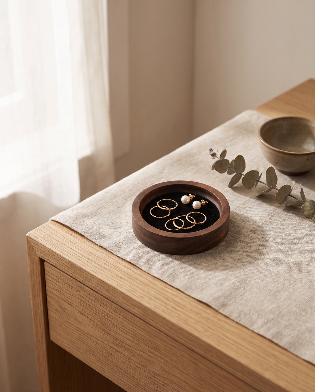 Small round walnut jewelry tray with black velvet insert, holding rings and a pearl